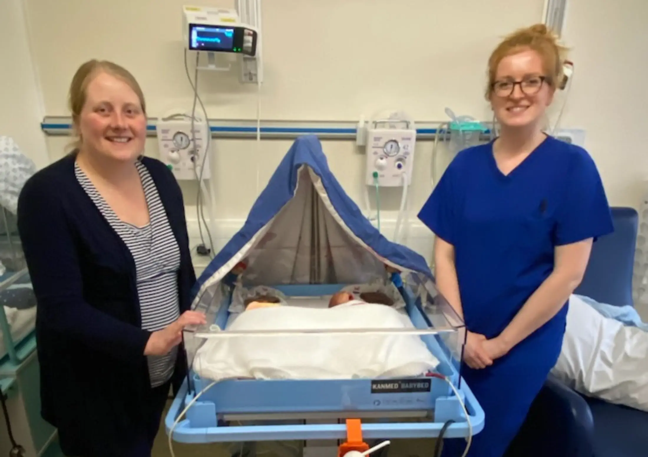 Parent and Nurse next to a Kanmed twin bed on a neonatal unit.