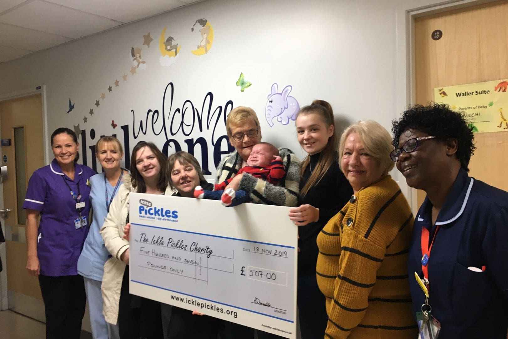 Newborn baby and family with maternity staff in a neonatal unit with a cheque for the Ickle Pickles Charity